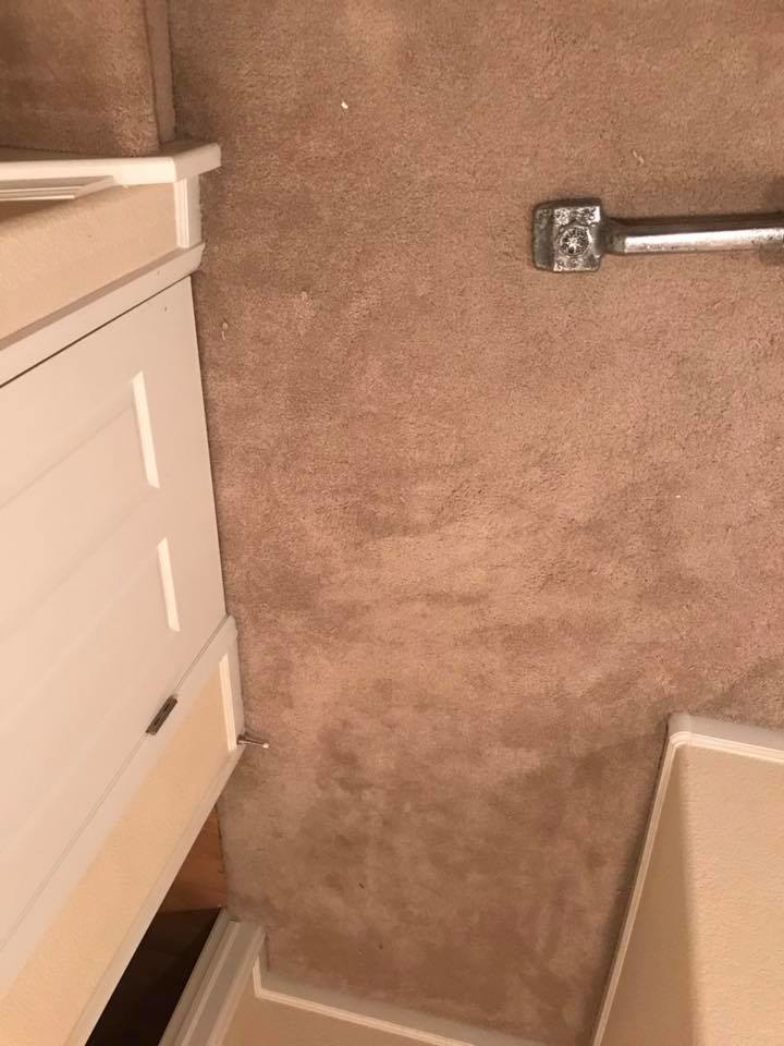 A carpet stretcher tool positioned on a carpet next to a white cabinet by Brett's Pro Carpet Repair in Fort Collins, CO.