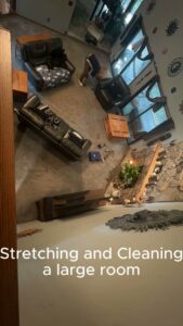 A professional stretching and cleaning carpet in a large room, demonstrating services by Hughes Dry Professional Carpet Care in Marietta, GA.