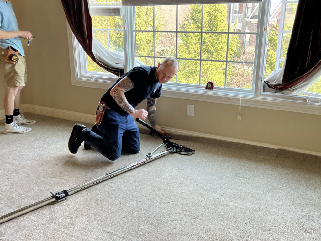 A carpet contractor using a power stretcher to install or repair carpet along a wall, performed by Mella Services in Covington, KY.