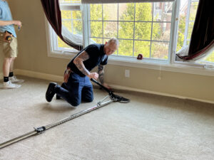 A carpet contractor using a power stretcher to install or repair carpet along a wall, performed by Mella Services in Covington, KY.