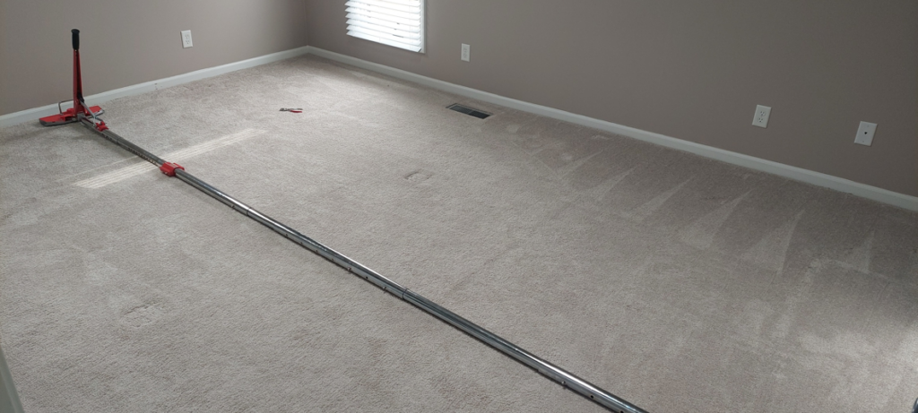 A carpet stretching tool positioned on a light-colored carpet in a room, indicating carpet repair work by Proper Carpet Cleaning in Aurora, IL.