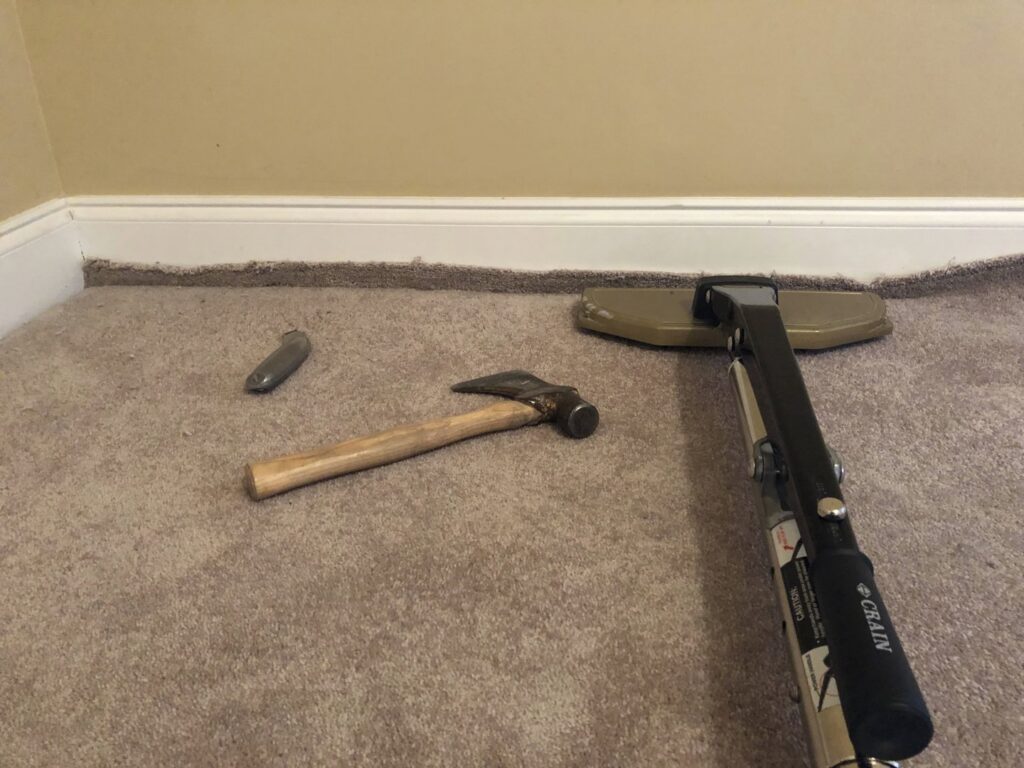 Carpet stretching tools, including a power stretcher and hammer, laid out on a carpet for a job by Fletcher's Carpet Cleaning & Stretching in Knoxville, TN.
