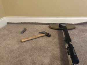 Carpet stretching tools, including a power stretcher and hammer, laid out on a carpet for a job by Fletcher's Carpet Cleaning & Stretching in Knoxville, TN.