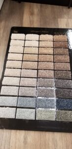 A display board showcasing various carpet swatches and textures at All Surfaces Wholesale in Houston, TX.