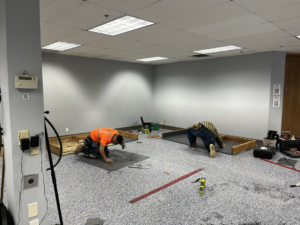 Two skilled workers kneeling and actively installing carpet tiles for a client by Hank's Specialties, Inc. in Saint Paul, MN.
