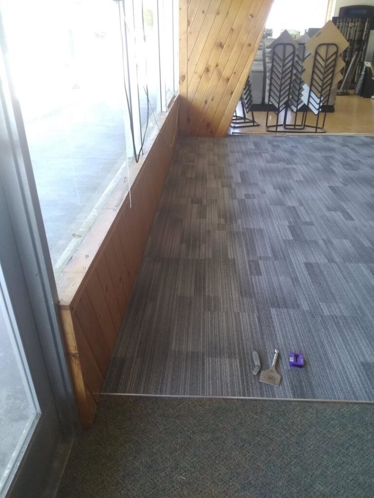 Carpet tile installation in progress with tools visible near a window by Carpet Center in Wilmington, NC.
