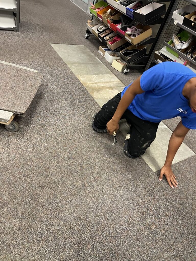 A worker installing carpet tiles in a retail store by Global Flooring Enterprise in Miami, FL.