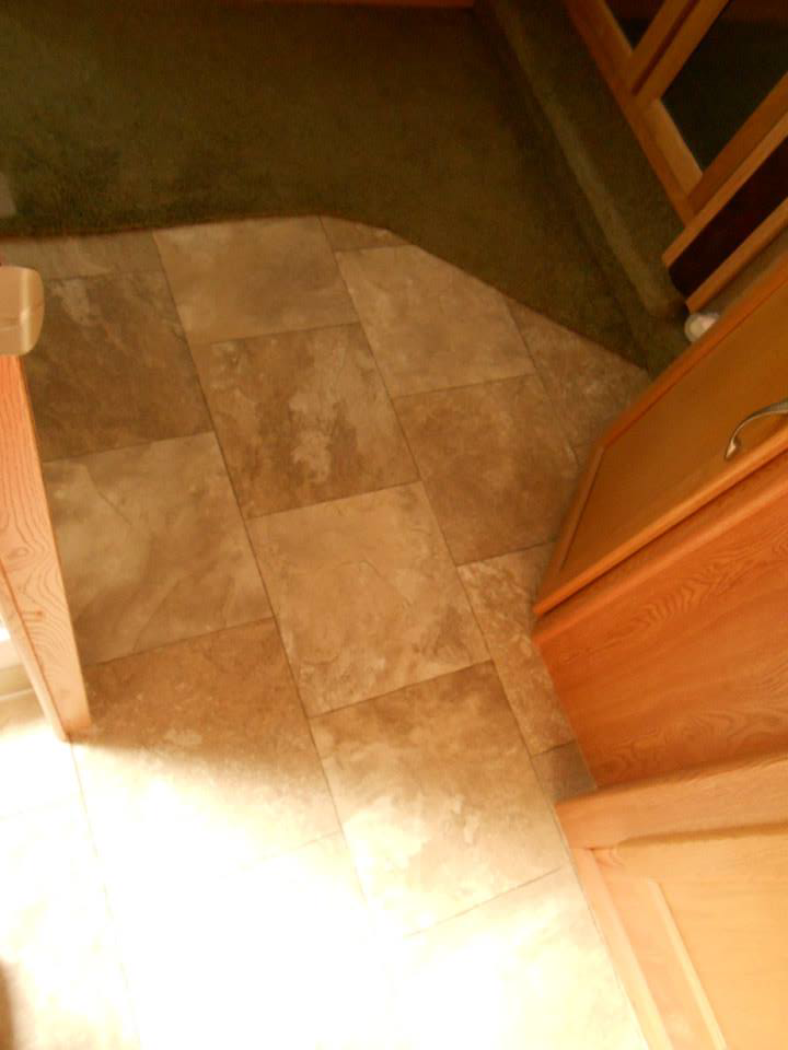 A seamless transition from green carpet to light brown tile-patterned vinyl flooring installed by Frosty's Carpet Center, Inc. in Grand Forks, ND.