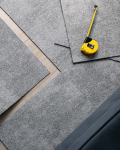Grey carpet tiles and a yellow measuring tape laid out, ready for installation by Gator Carpet and Tile in Jacksonville, FL.