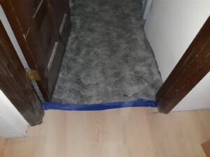 A close-up of a newly installed gray patterned carpet transitioning to light hardwood flooring at a doorway by Advanced M&D Sales, Inc. in Portland, OR.