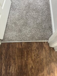 A close-up view of a clean transition from new carpet to hardwood flooring, installed by Floors To Go in Virginia Beach, VA.