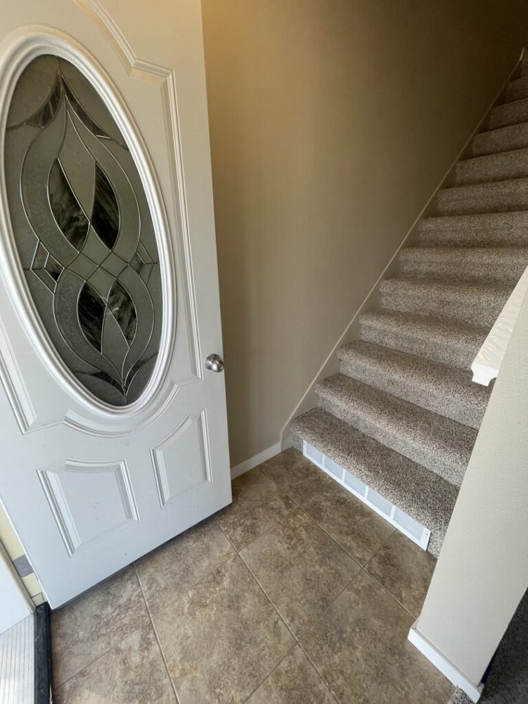 Carpeted stairs leading from an entryway with tile flooring, installed by Rayman Flooring in Aberdeen, SD