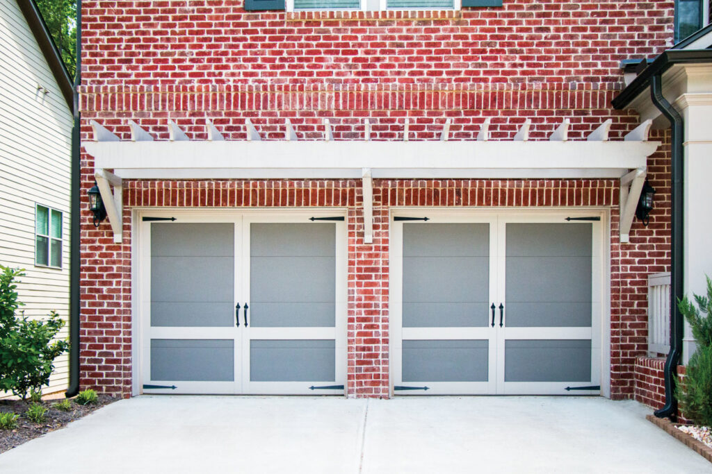 Two custom carriage-style garage doors with decorative hardware on a brick home by American Overhead Door in Madison, AL