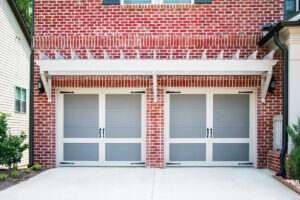 Two custom carriage-style garage doors with decorative hardware on a brick home by American Overhead Door in Madison, AL