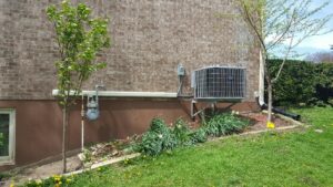 A Carrier air conditioning unit installed on a wall bracket next to a brick house by Custom Climates in Iowa City, IA.