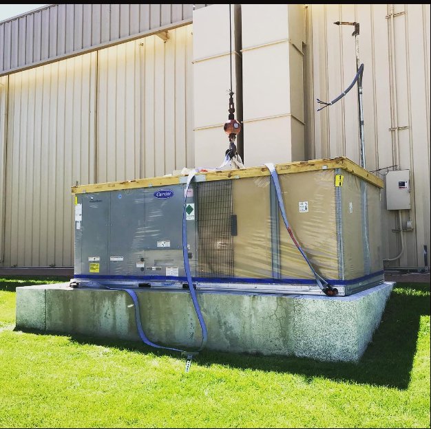 A new Carrier commercial HVAC unit being installed by crane onto a concrete pad by CHAMPS Heating&Air in Denver, CO