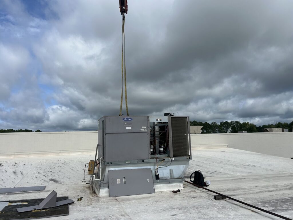 A Carrier commercial rooftop HVAC unit being lifted by a crane onto a building by Underwood Heating and Air Conditioning in Phenix City, AL