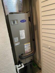 An indoor Carrier furnace or air handler unit installed in a utility closet by JM HVAC Pros in Elgin, IL.