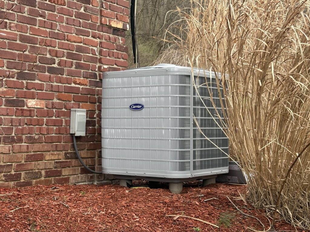 An outdoor Carrier HVAC unit installed next to a brick building, serviced by Delgado Enterprises in Pittsburgh, PA