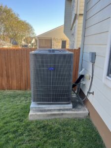A Carrier outdoor AC condenser unit installed next to a residential fence by South Texas Climate Control in San Antonio, TX
