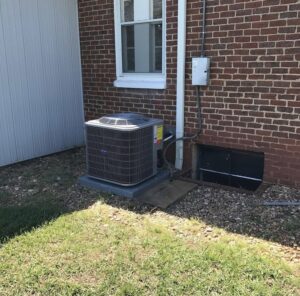 A Carrier outdoor HVAC condenser unit installed next to a brick house by Systematic Heating & Air in Winston-Salem, NC.