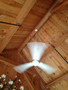 A spinning ceiling fan with lights installed on a wooden ceiling with exposed conduit by RightWay Electric RI in Providence, RI.