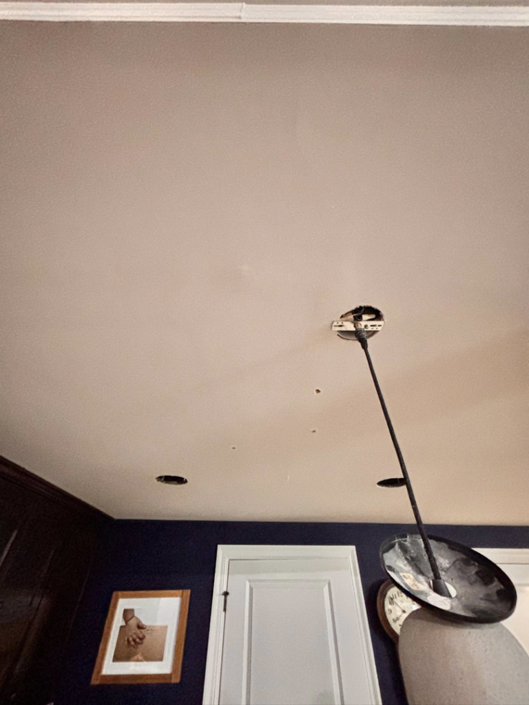 An electrician installing a ceiling light fixture and recessed lighting in a home by 3 Phase KC in Independence, MO.