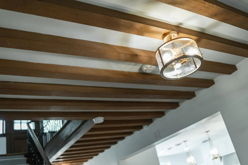 A ceiling with exposed beams showcasing a modern light fixture and smoke detector installed by Power Plus Electric LLC in Rochester, MN.