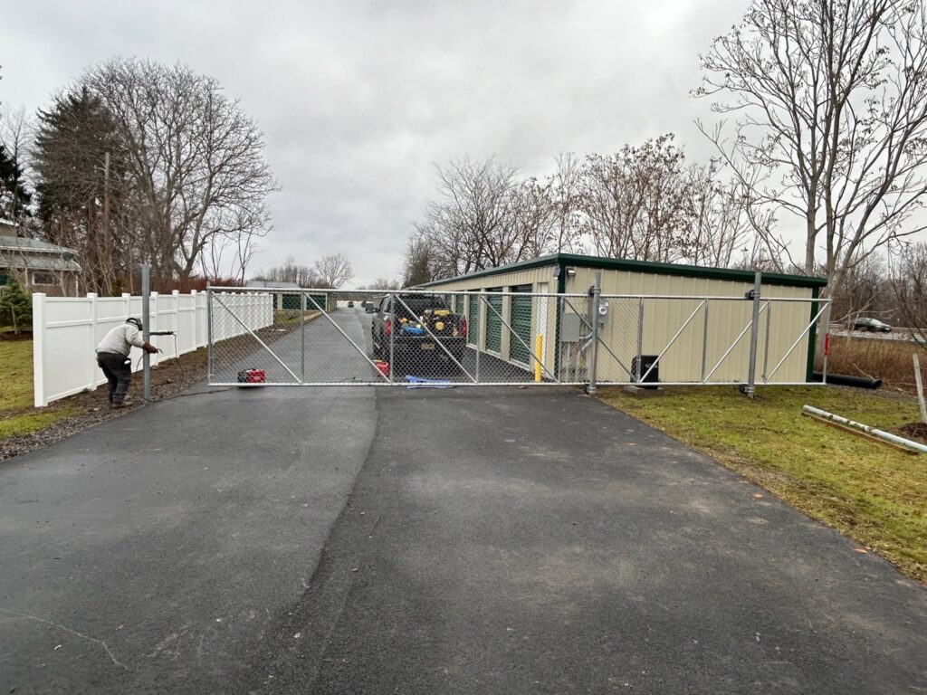 A worker installing a chain-link fence alongside a white vinyl fence by Camp Carlson Fencing in Rochester, NY.