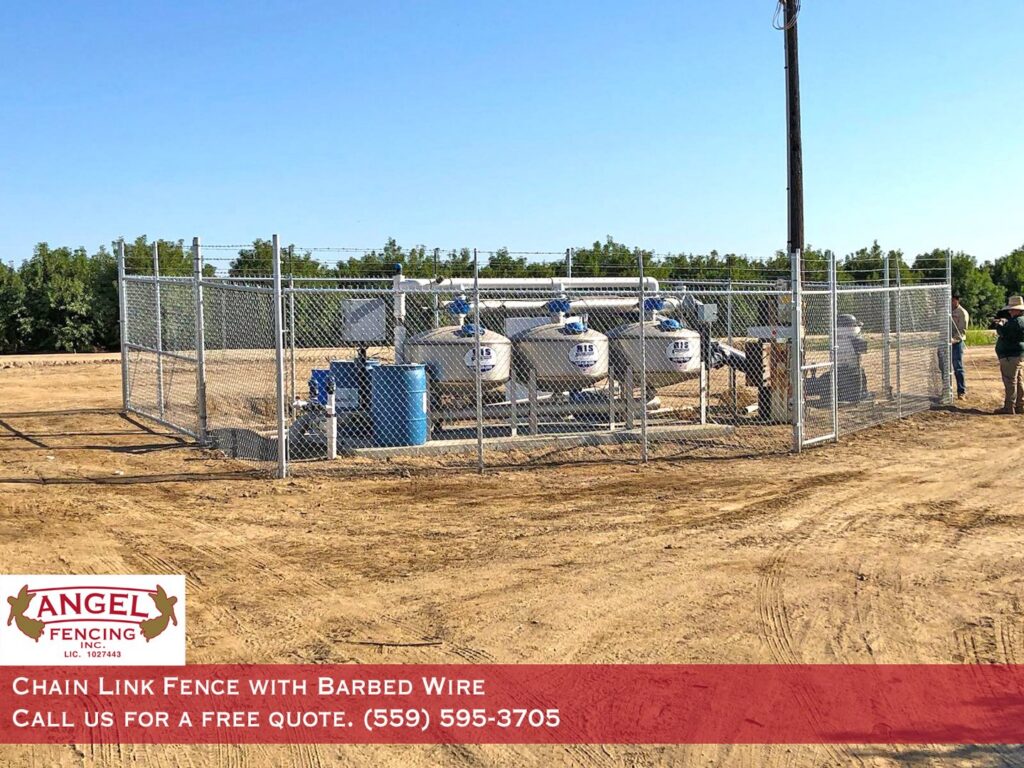 A chain link fence with barbed wire around industrial equipment installed by Angel Fencing Inc. in Fresno, CA
