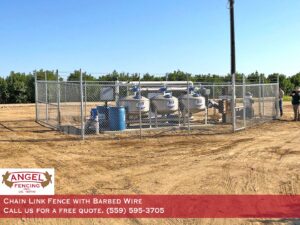 A chain link fence with barbed wire around industrial equipment installed by Angel Fencing Inc. in Fresno, CA