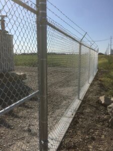 A chain-link fence with barbed wire installed around a utility area by Schumacher Fencing, LLC in Columbus, NE.