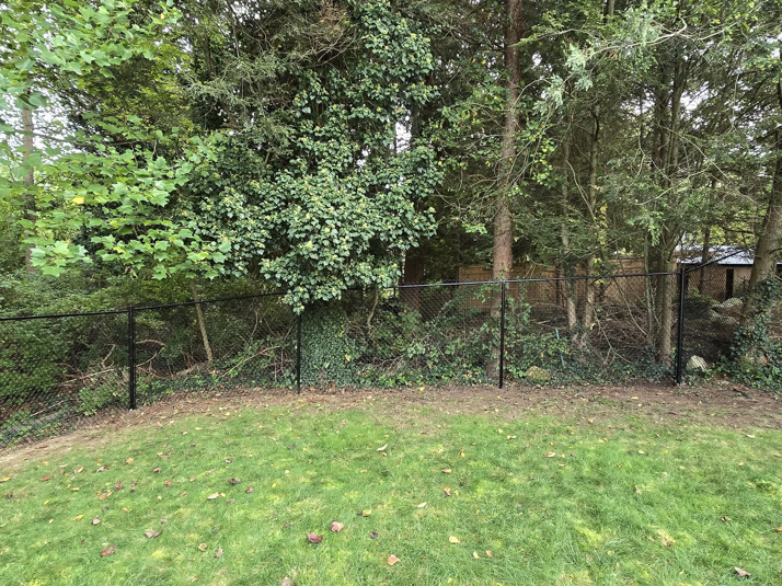 A black chain-link fence installed along a property line, viewed from a grassy lawn by Homestead Fence in Cumberland, RI.