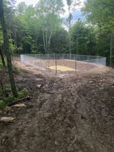 A newly installed chain-link fence enclosing a pond or basin in a wooded area by Stapleton Fencing LLC in Lexington, KY.