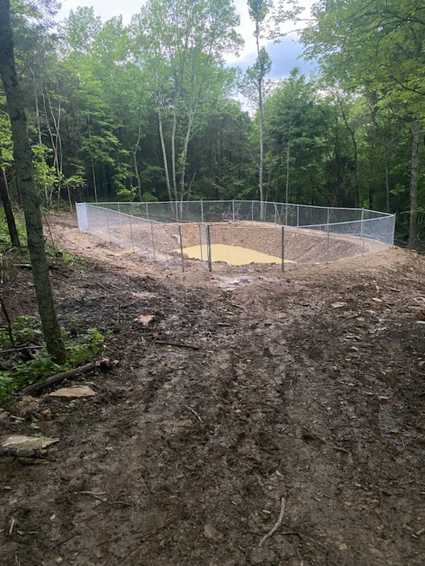 A newly installed chain-link fence enclosing a pond or basin in a wooded area by Stapleton Fencing LLC in Lexington, KY.