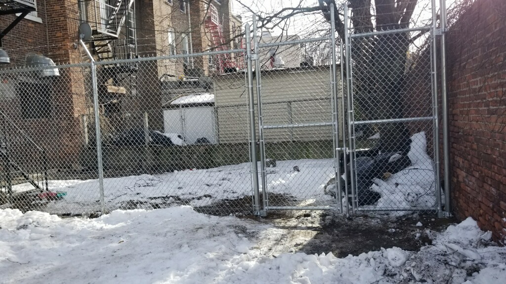 A chain-link fence with double gates installed in a snowy backyard, completed by Fox Fence Enterprises Inc in Clifton, NJ.