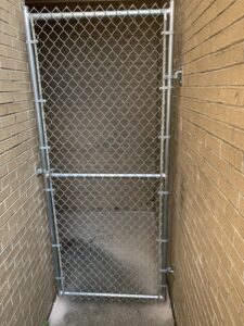 A chain-link fence gate installed in a narrow alleyway between brick buildings by Pride Fence LLC in Overland Park, KS.