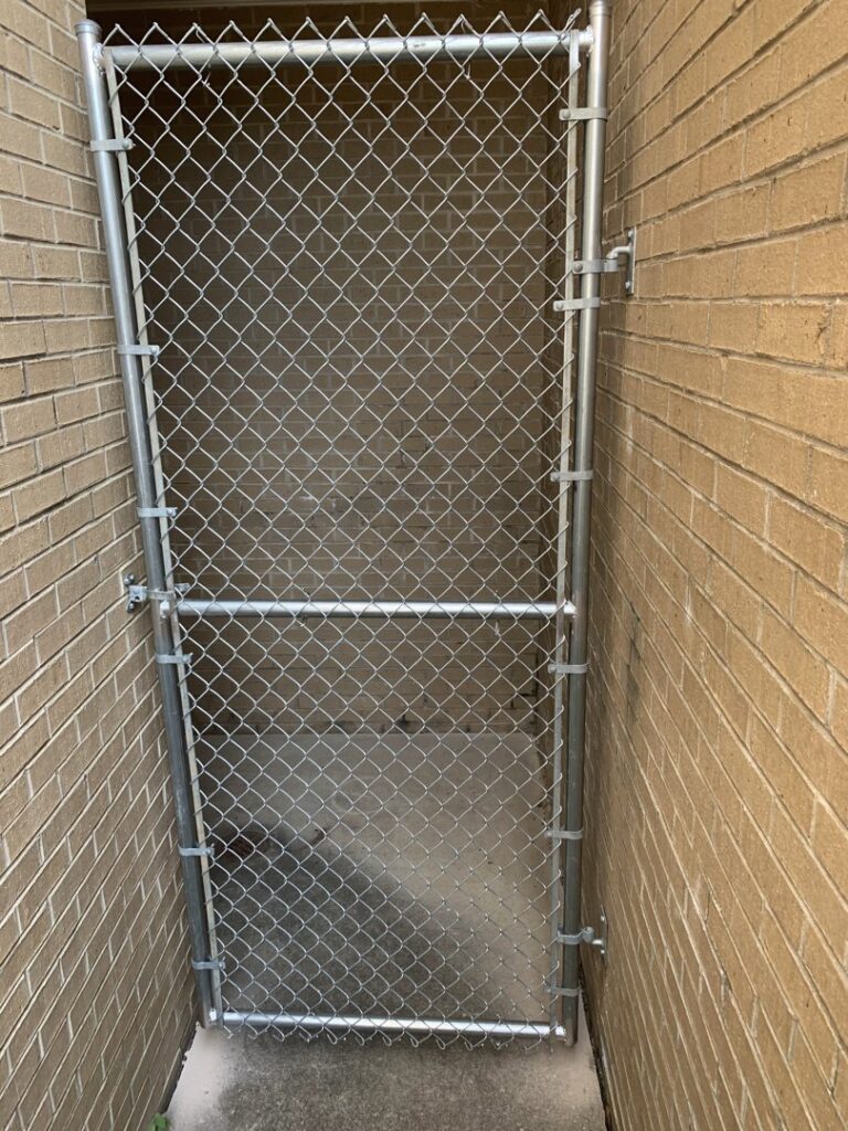 A chain-link fence gate installed in a narrow alleyway between brick buildings by Pride Fence LLC in Overland Park, KS.