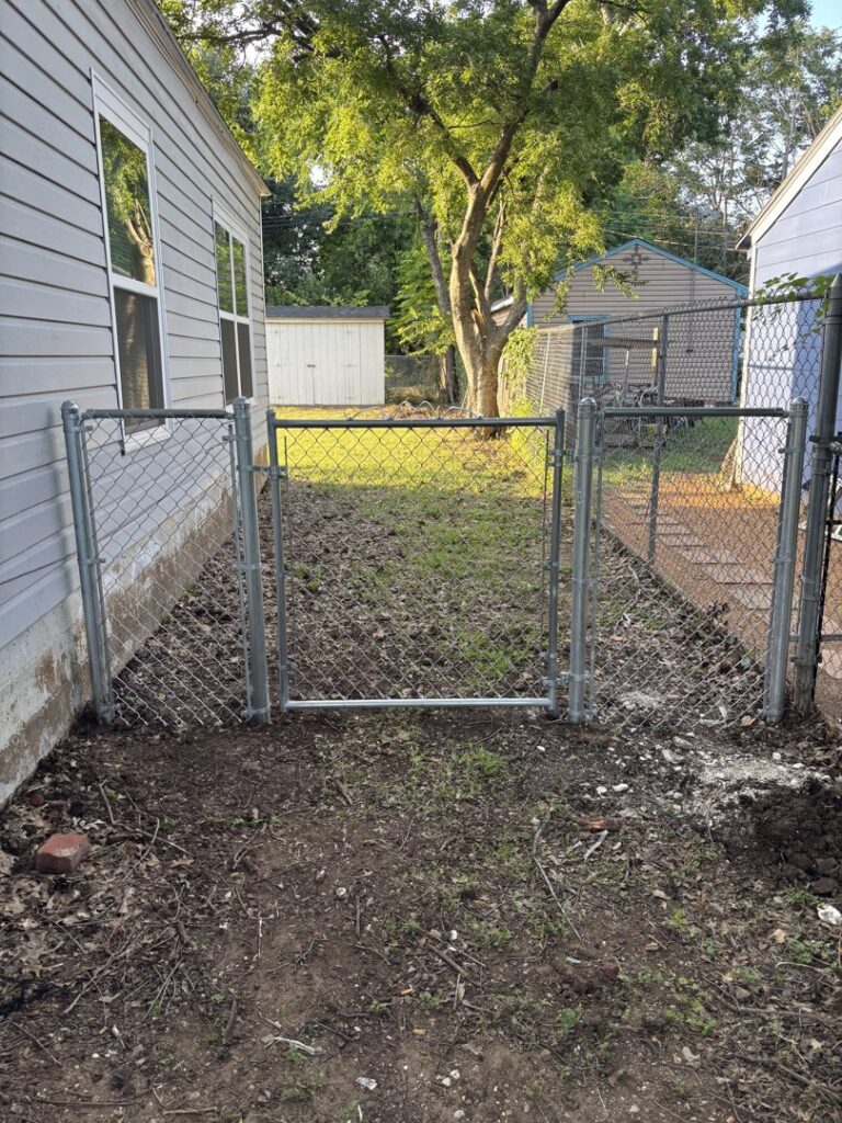 A chain-link fence gate installed in a narrow side yard between two houses by Dallas Fence in Dallas, TX.