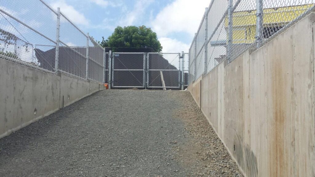 A chain-link fence and gate installed at the bottom of a sloped concrete path by David's Fencing Inc. in Waipahu, HI.