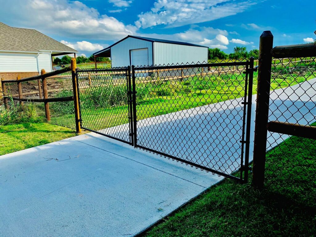 A black chain link fence gate with rustic wooden posts installed by Ninety-One Services in Tulsa, OK