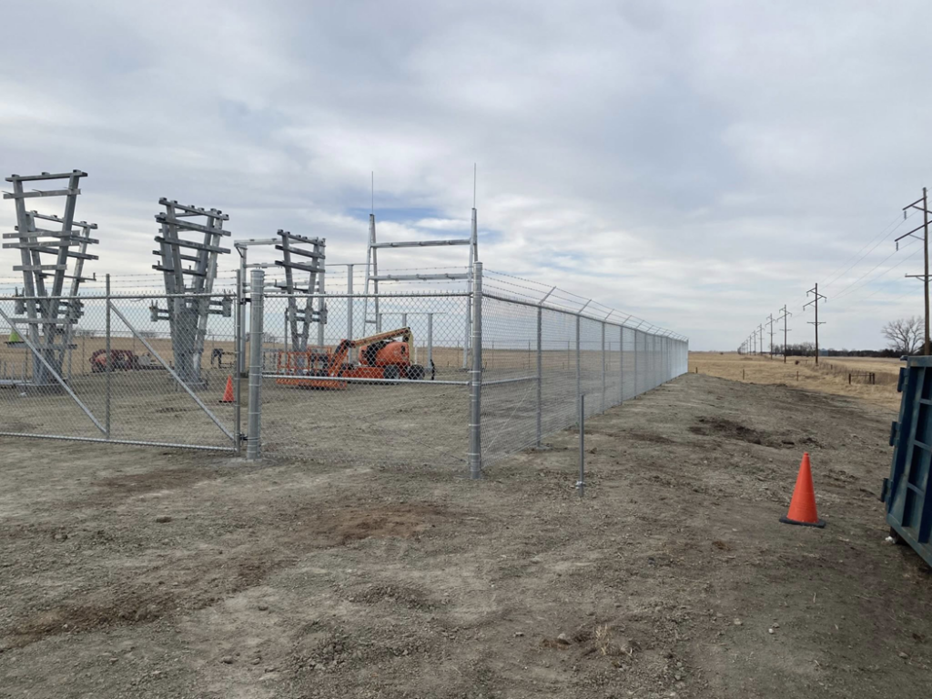 A newly installed chain-link fence with barbed wire enclosing an electrical substation by Big Red Fencing LLC in Waverly, NE.