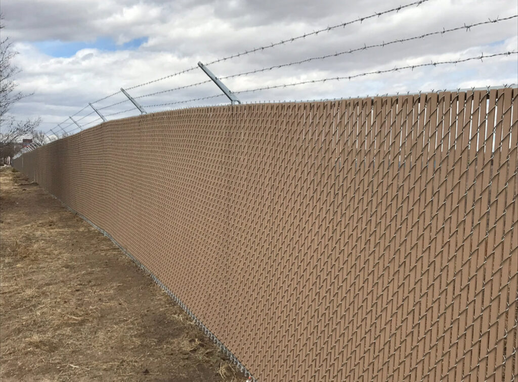 A long chain-link fence with privacy slats and barbed wire, installed by Colorado Springs Fence Company in Colorado Springs, CO.