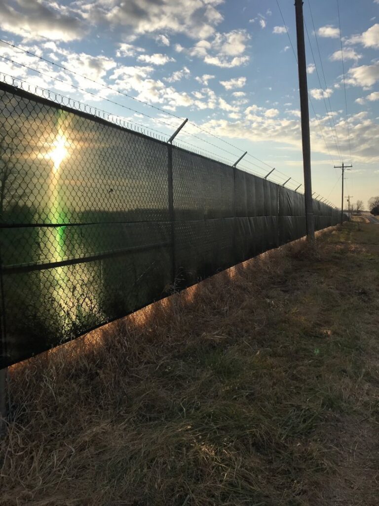 A long chain-link fence with privacy slats and barbed wire installed by Roy & Son Fencing in Lee's Summit, MO.