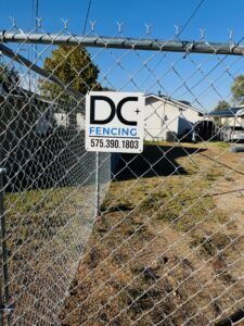 A newly installed chain-link fence featuring a DC Fencing LLC business sign, showcasing work in Clovis, NM.