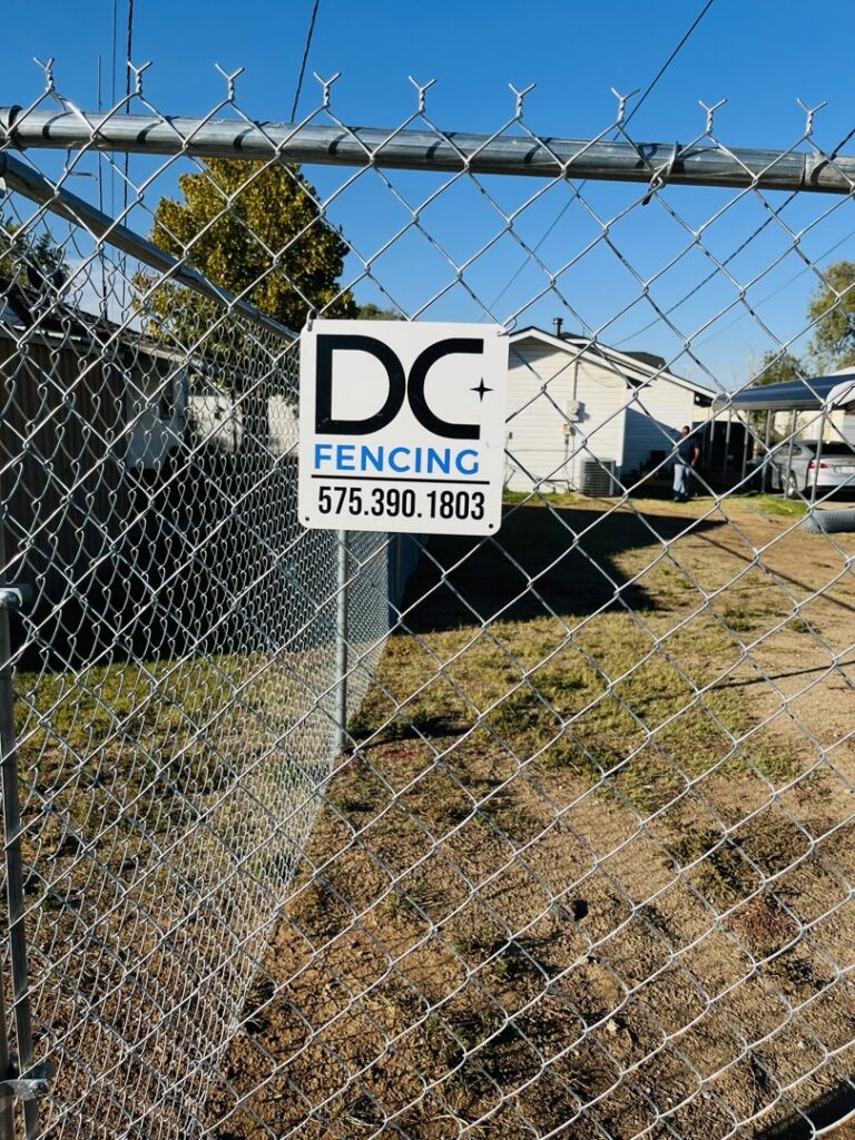 A newly installed chain-link fence featuring a DC Fencing LLC business sign, showcasing work in Clovis, NM.