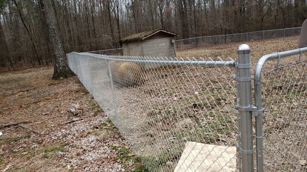 A chain-link fence with a gate in a natural, open area by Fences & Landscape Inc in Little Rock, AR.
