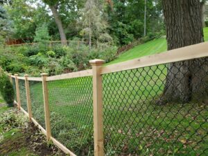 A black chain-link fence with wooden posts and top rail on a sloped lawn by Top Notch Fence in East Bethel, MN