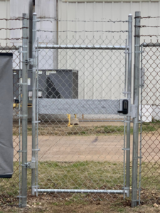 A close-up of a chain-link fence gate with a keypad lock and diamond plate reinforcement installed by BAR Z Fencing and Welding LLC in Midlothian, TX