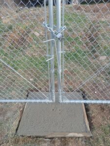 A close-up of a chain-link gate post with a lock and concrete base installed by DB Fencing, LLC in Teague, TX.
